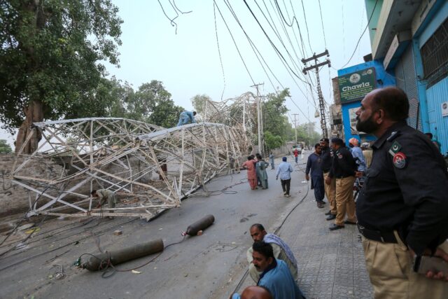 A policemen looks on as workers remove a fallen tower after a violent storm in Multan, Pak