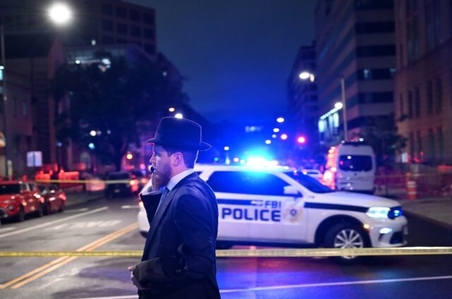 A man, standing behind police tape, talks on his cell phone outside the Capital Jewish Mus