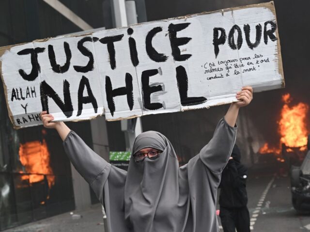 TOPSHOT-FRANCE-CRIME-POLICE-DEMO TOPSHOT - An attendee holds a banner reading "Justice for Nahel" as cars burn in