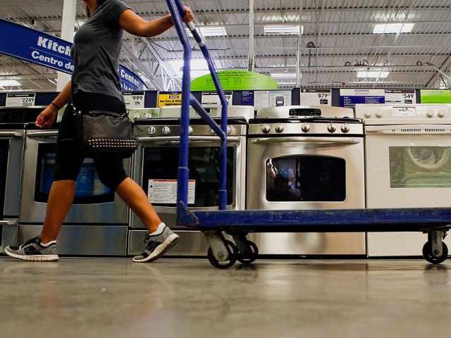 A woman pulls a cart past a General Electric Co. gas range and oven, center, displayed for