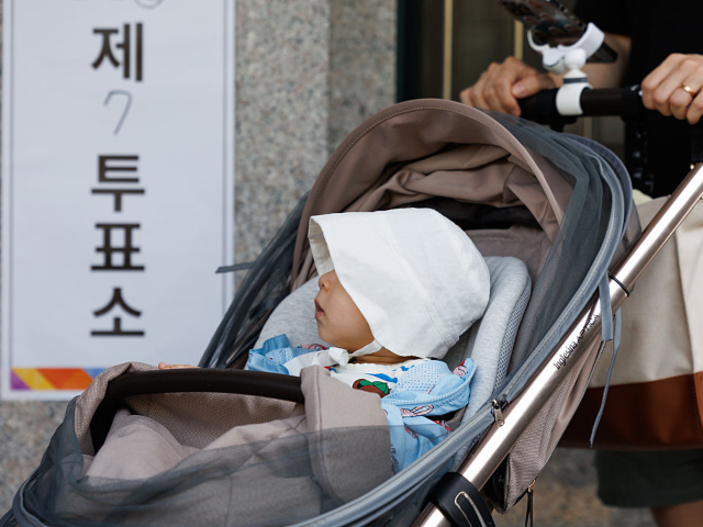 GettyImages-2217736501 An infant in a stroller in the line at a polling station during the presidential election