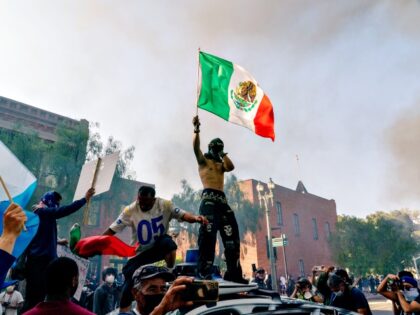 Protesters stand on top of a destroyed vehicle in Los Angeles, California, US, on Sunday,