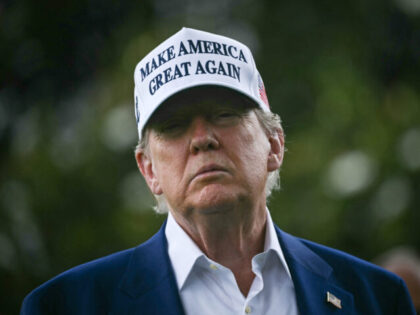 TOPSHOT - US President Donald Trump speaks to the press as workers install a large flag po