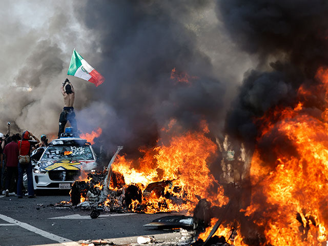A protestor holds up a Mexican flag as burning cars line the street on June 08, 2025 in Lo
