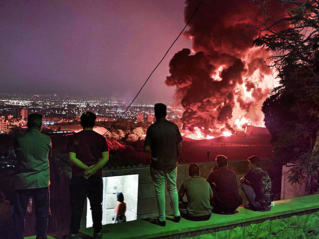 People observe fire and smoke from an Israeli attack on the Shahran oil depot on June 15,