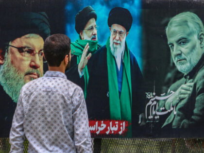 A man looks at a billboard featuring the portraits of (Left to Right) Hassan Nasrallah, th