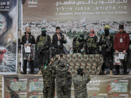 Hamas and Islamic Jihad militants stand next to Russian-Israeli hostage Sasha Alexander Tr