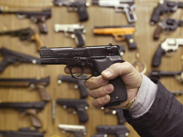A man holds an Airsoft plastic BB gun in front of a shop display of the hobbyist replica f