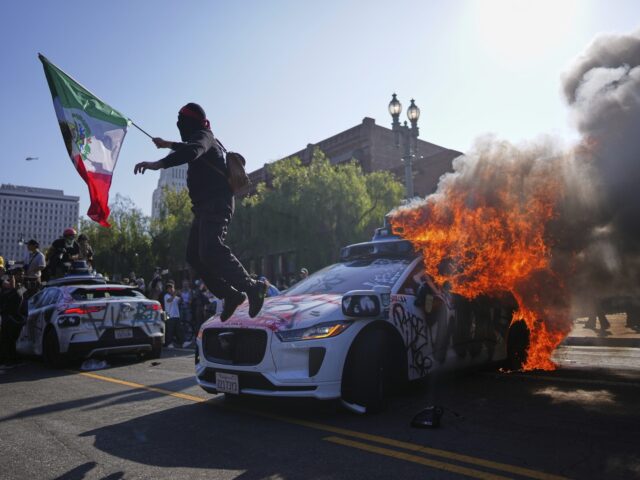 A protester leaps off a burning Waymo taxi near the Metropolitan Detention Center in downt