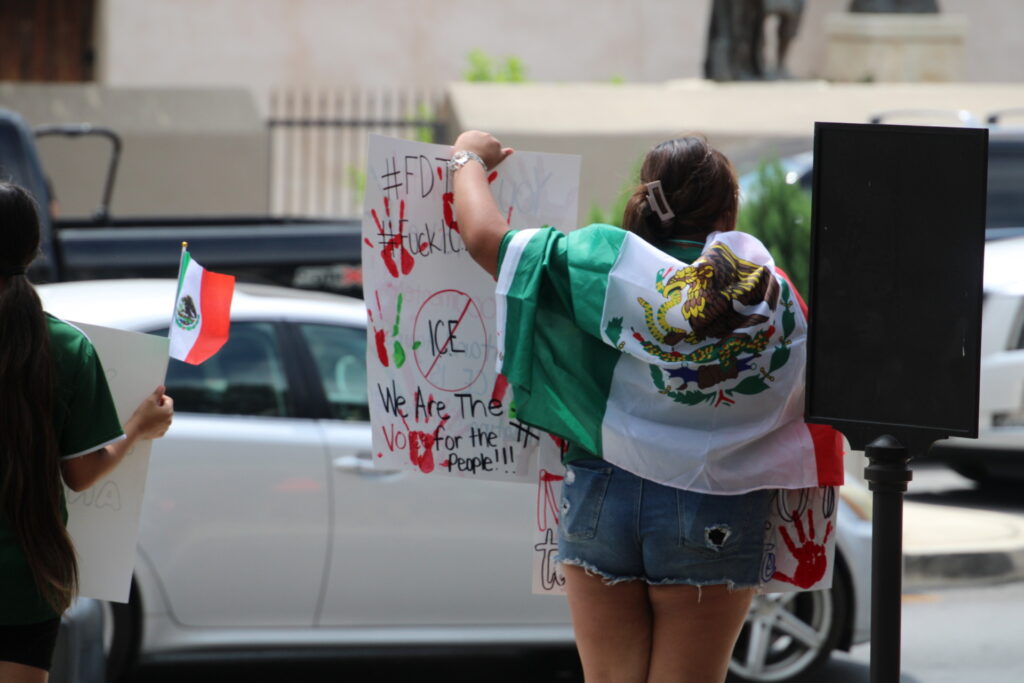 Para pengunjuk rasa yang dibungkus dengan bendera Meksiko membawa tanda dengan pesan vulgar di Reli Anti-Ice, Foto oleh Randy Clark (Randy Clark/Breitbart Texas)