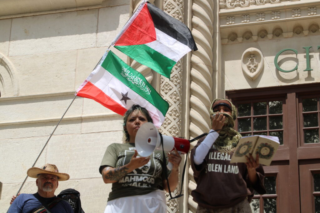 Para pengunjuk rasa membaca Anti-Israel, pesan anti-es di sebelah bendera Palestina di foto protes anti-es oleh Randy Clark (Randy Clark/Breitbart Texas)