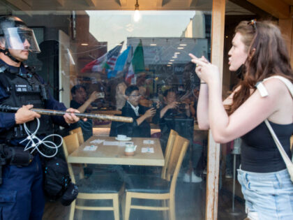 Diners in a restaurant look on as a protester gestures toward a police officer in riot dur