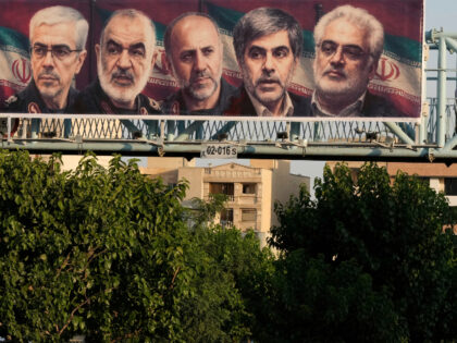 A man walks past a billboard displaying images of top Iranian commanders and scientists ki