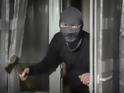 Thief with an ax in his hand and in a hat with a slit for the eyes sneaks into the house t