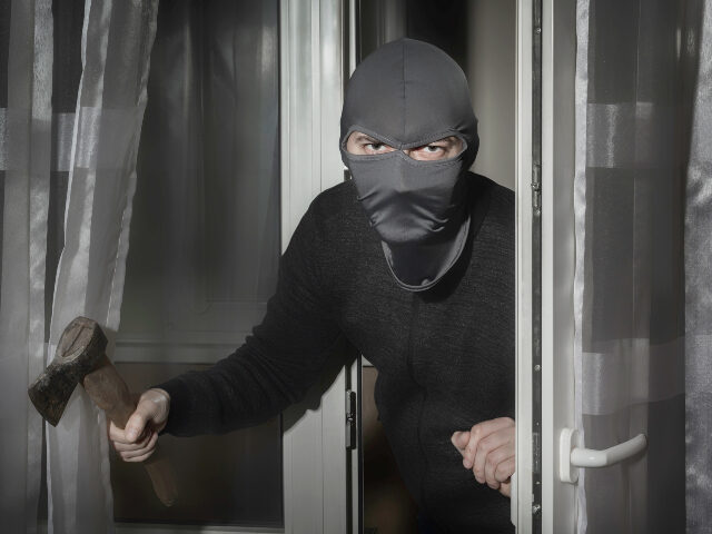 axe-wielding intruder Thief with an ax in his hand and in a hat with a slit for the eyes sneaks into the house t