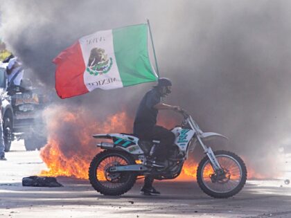 A demonstrator waves a Mexican national flag next to a car on fire during a protest follow