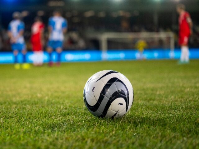 Football kept on grassy football pitch.