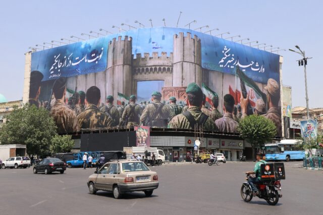 Iranians drive past an anti-Israel poster in Tehran's Enghlab Square