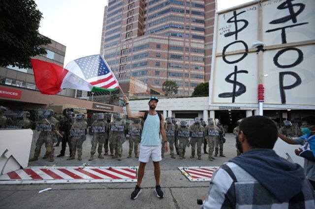 A man stands in front of a row of California National Guard members and waves a combinatio