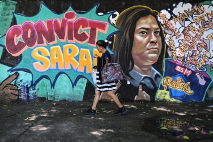 A woman walks past a mural calling for the conviction of Philippine Vice President Sara Du