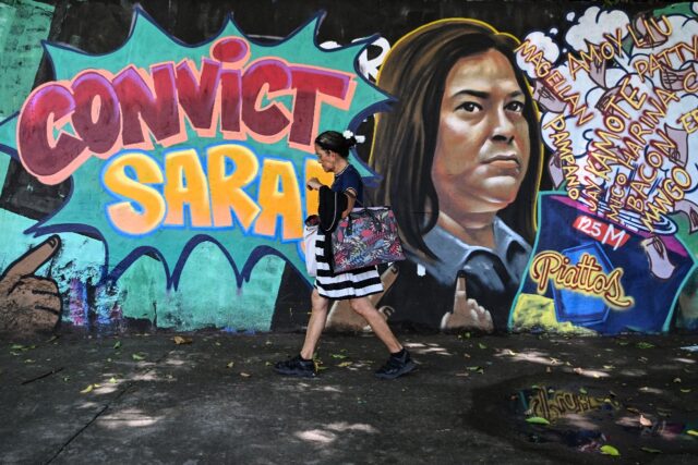 A woman walks past a mural calling for the conviction of Philippine Vice President Sara Du