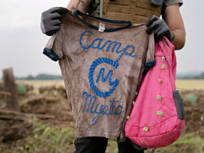 A search and rescue volunteer holds a T-shirt and backpack with the words Camp Mystic on t