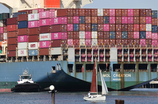LOS ANGELES, CALIFORNIA - JUNE 25: A sailboat passes shipping containers stacked on a cont