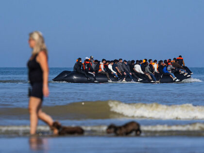 TOPSHOT - A tourist walks her dogs as migrants board a smuggler's boat in an attempt