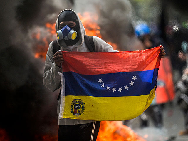 A hooded demonstrator holds a national flag near a burning motorbike during a protest agai