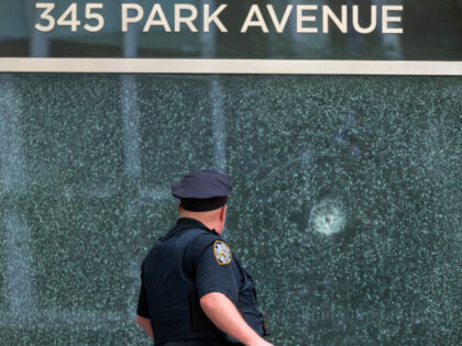A New York Police Department (NYPD) officer stands in front of a bullet-shattered window a