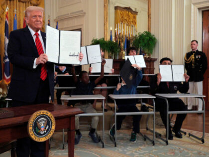 U.S. President Donald Trump, joined by school children, holds up an executive order reduci
