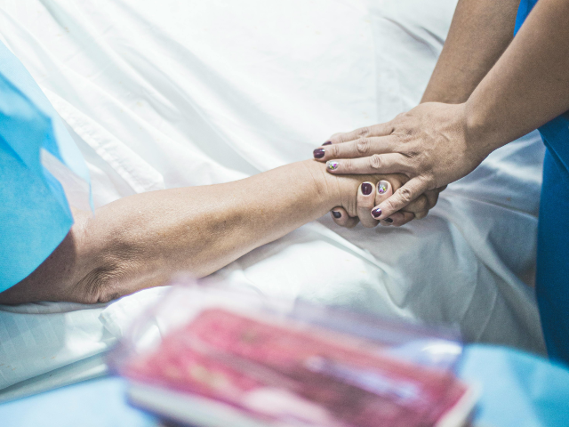 pexels-daliladalprat-5875563 Person in Blue Scrubs Holding the Hand of a Patient Lying on Bed