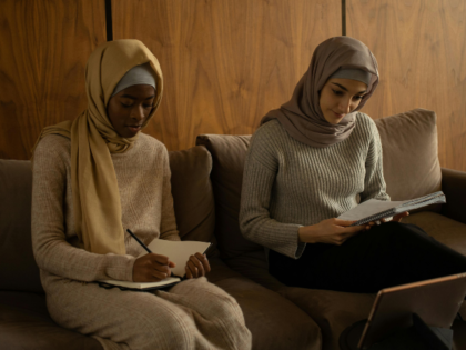 women in hijabs writing in copybooks while sitting on couch
