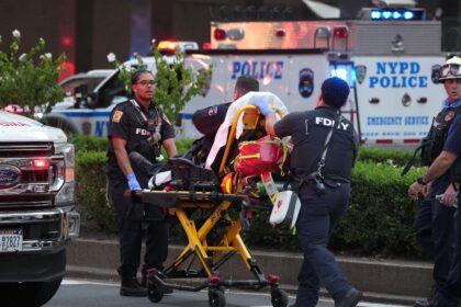 Firefighters wheel a police officer on a gurney as police respond to an incident in the Mi