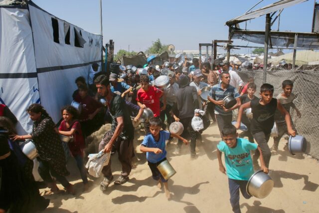 Palestinians rush to queue at a charity kitchen in Gaza, where the population has been exp
