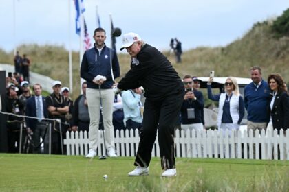US President Donald Trump, watched by his son Eric Trump, drives off the first tee to offi