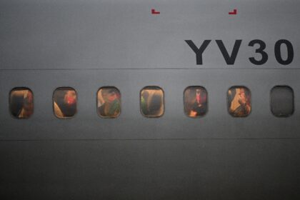 Venezuelan migrants who were jailed in El Salvador peer out the windows of the plane as it