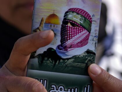 A demonstrator takes photos with her mobile phone covered with a picture of Abu Obeida, th