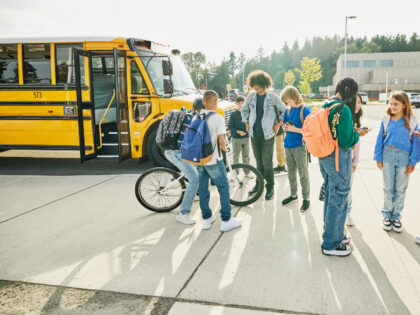 Wide shot of middle school students hanging out and looking at phones after school waiting