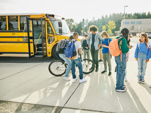 Children waiting for school bus Wide shot of middle school students hanging out and looking at phones after school waiting