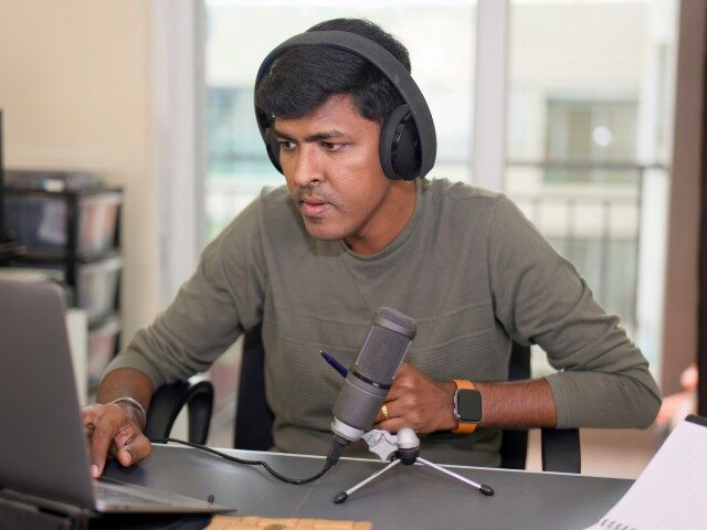 GettyImages-2162491519 Young man intensely recording a podcast, editing audio on his laptop with professional mic