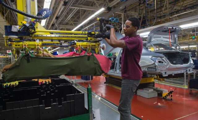 An employee uses a robotic arm to help lift intaernal parts for a Mercedes-Benz C-Class at
