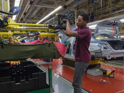 An employee uses a robotic arm to help lift intaernal parts for a Mercedes-Benz C-Class at