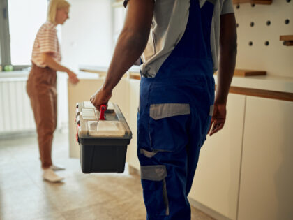 Black plumber in overalls with toolbox in hand came to customer’s home to solve problem