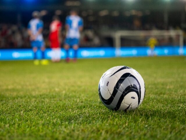 Football kept on grassy football pitch.