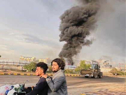People ride a motorbike as smoke billows following Israeli airstrikes on multiple areas in