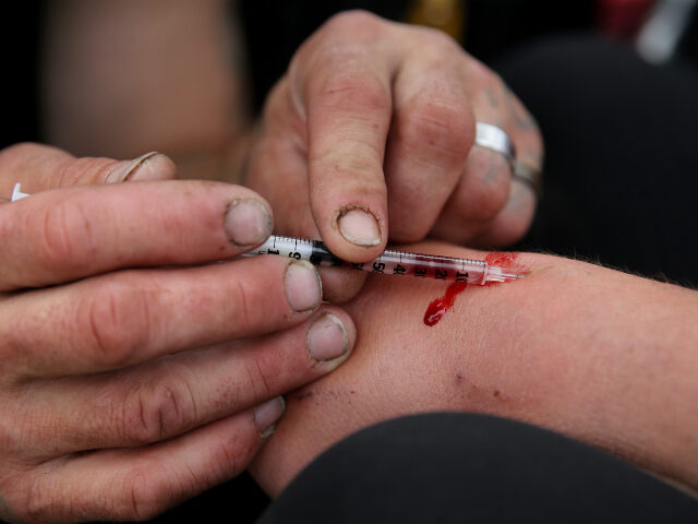 drugs, heroin A man helps a woman inject heroin into her wrist near a comfort station on Massachusetts A