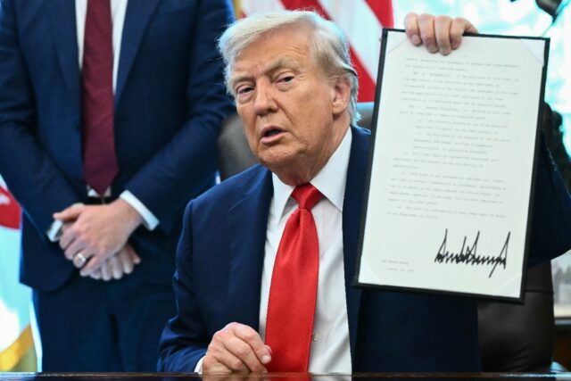 US President Donald Trump holds up an executive order in the Oval Office
