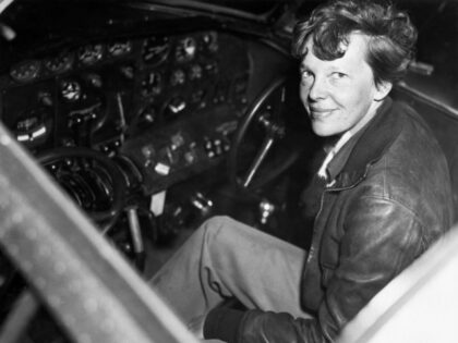 Amelia Earhart smiles as she sits clad in a leather aviator's jacket in the cockpit o