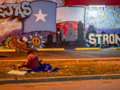 An unhoused person sits on the grass near a gas station on December 18, 2023 in Austin, Te